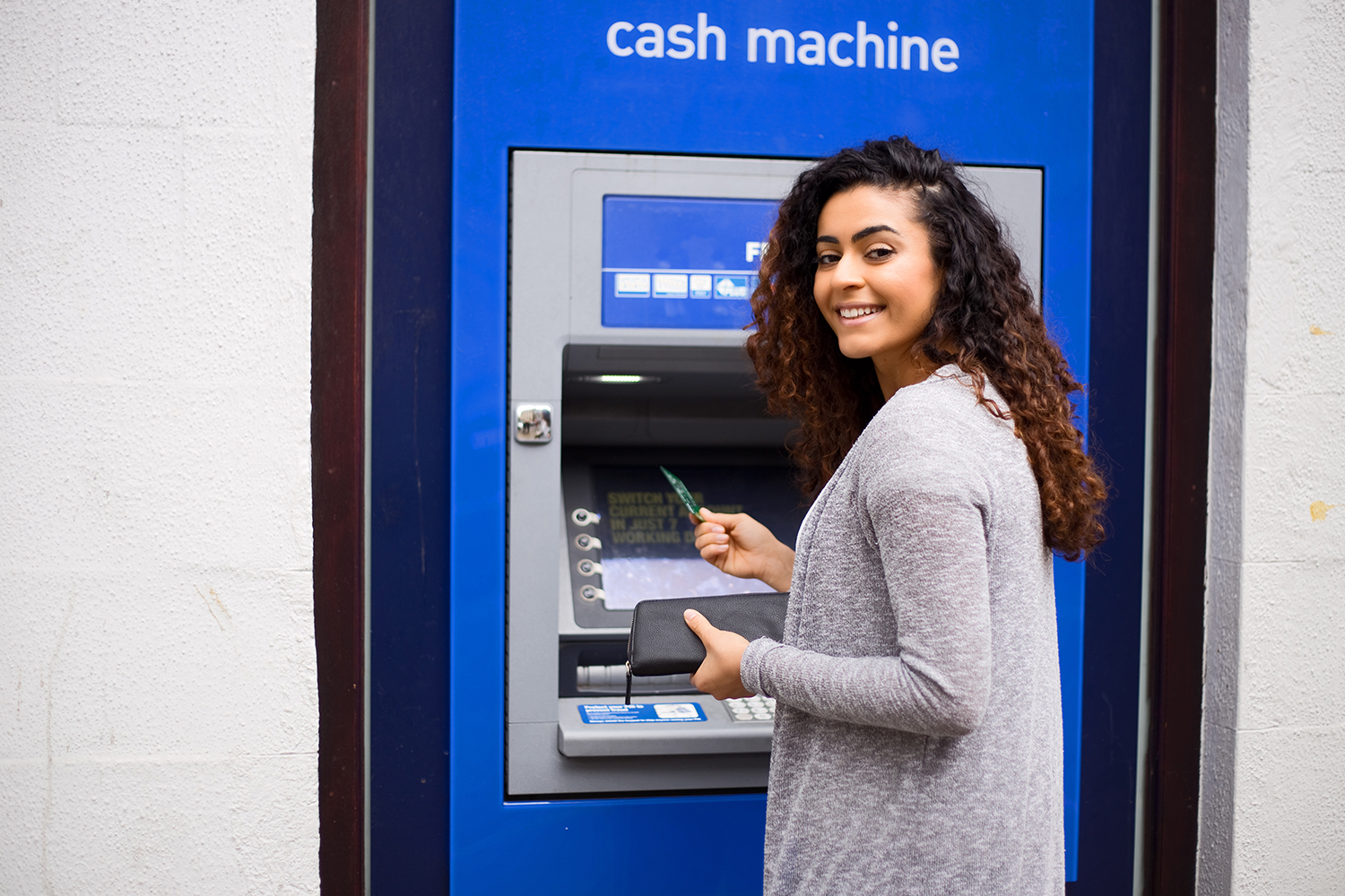 A woman using and ATM and smiling.