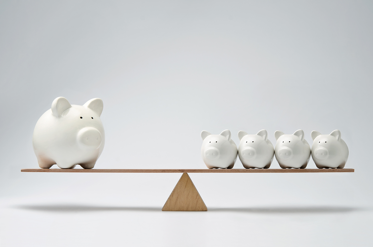 Five white piggy banks balanced on a wooden scale, symbolizing savings and financial management.