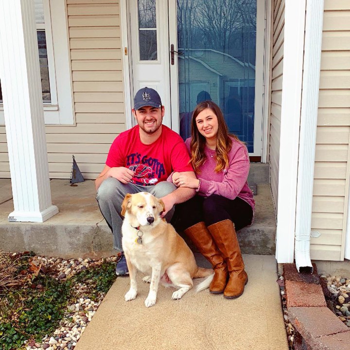 Two people sitting on the porch of their brand new home with their dog in front of them.