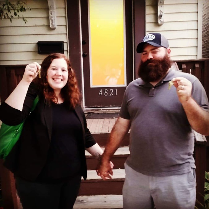 Two people standing in front of a new home holding up keys.