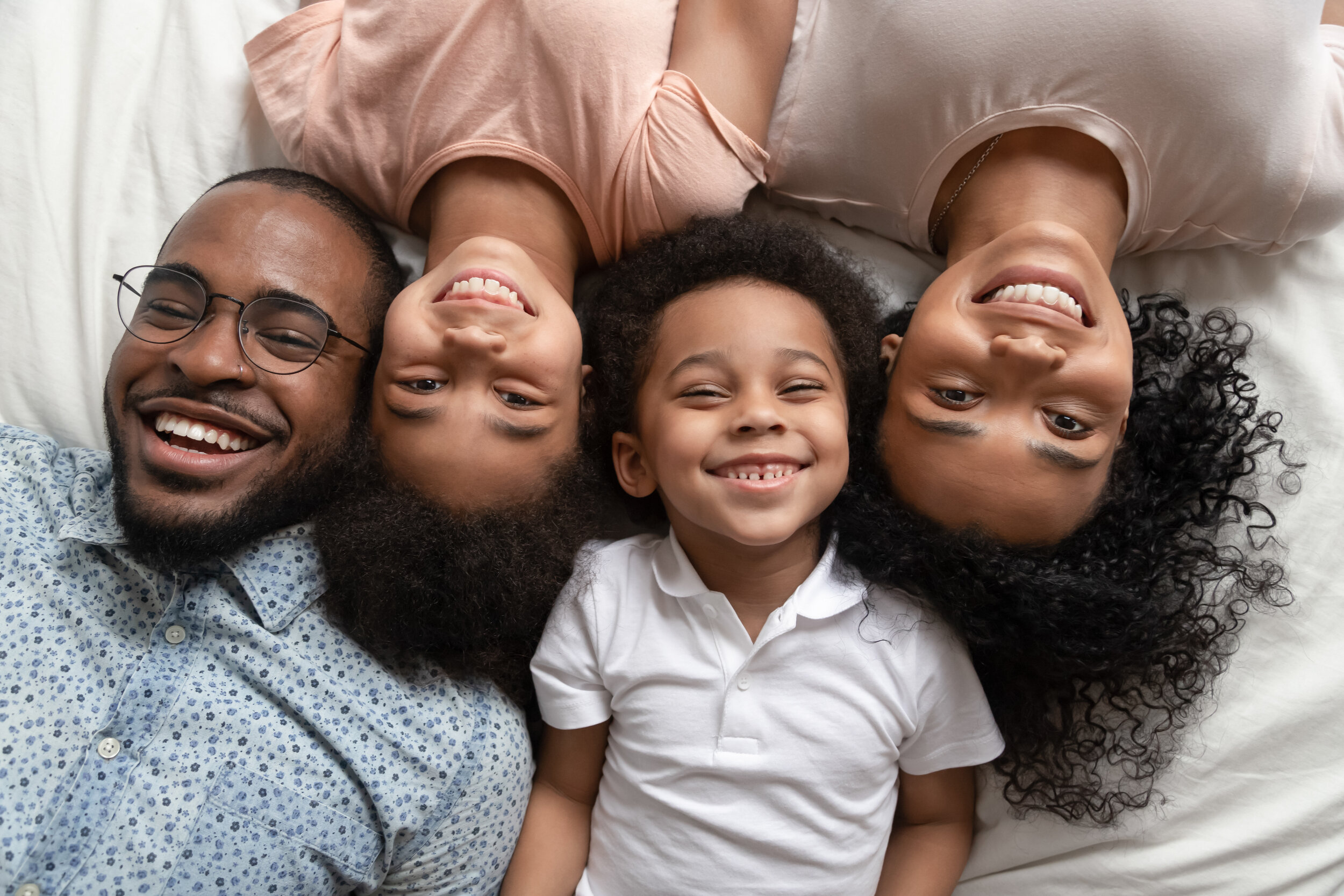 A family of four laying on a bed with their heads close together.