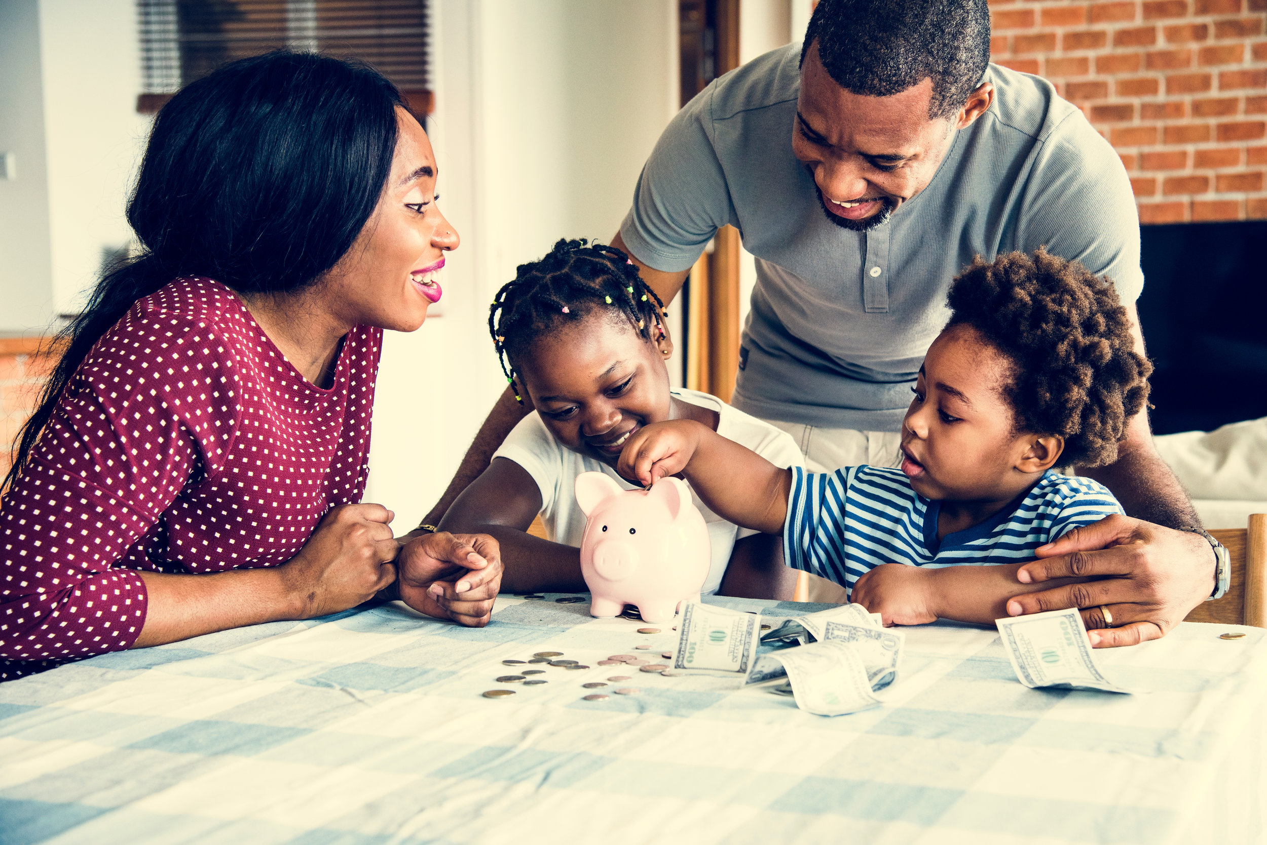 A family gathers around, happily inserting coins into a colorful piggy bank together.