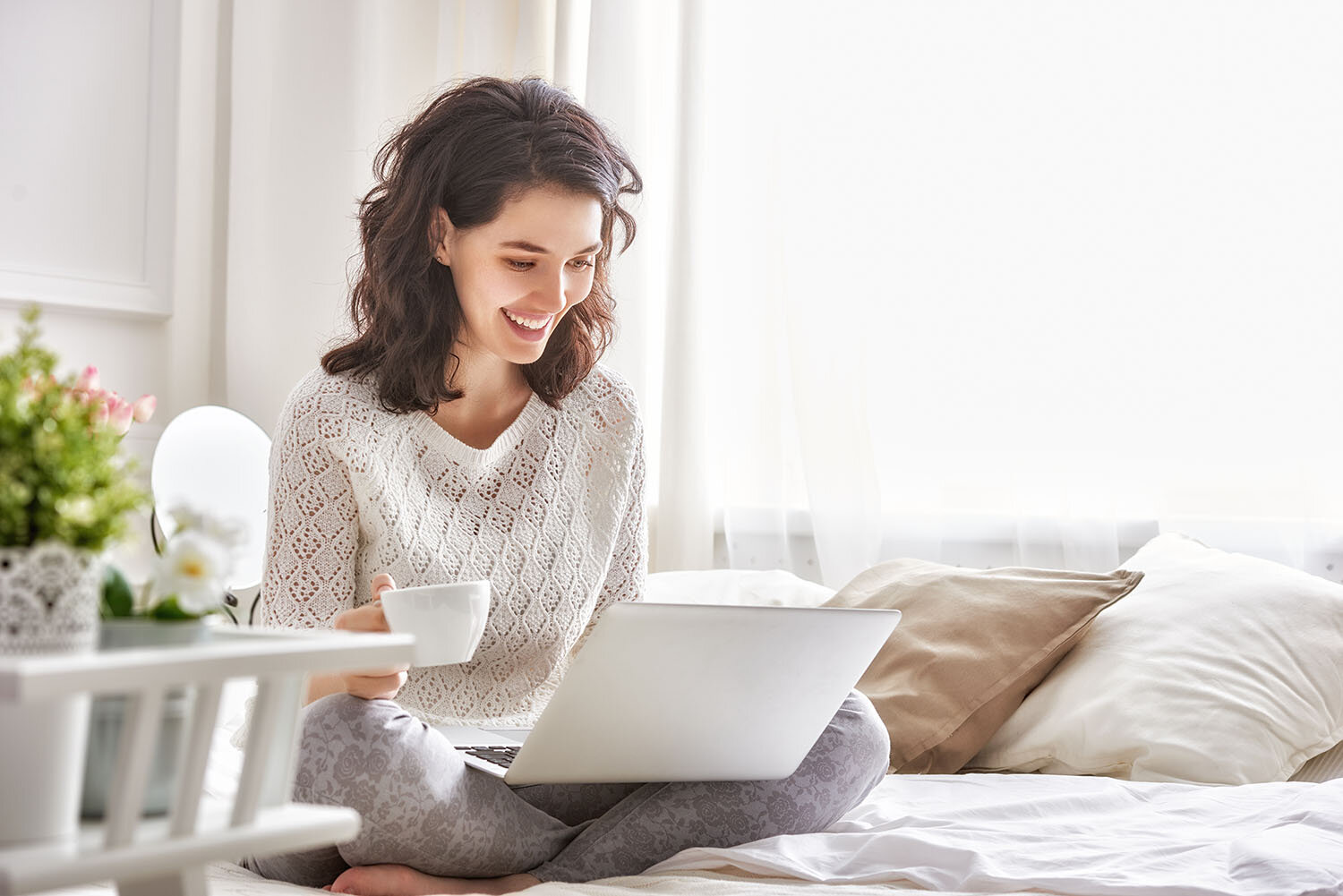 A woman sitting on a bed and smiling and a laptop computer screen.
