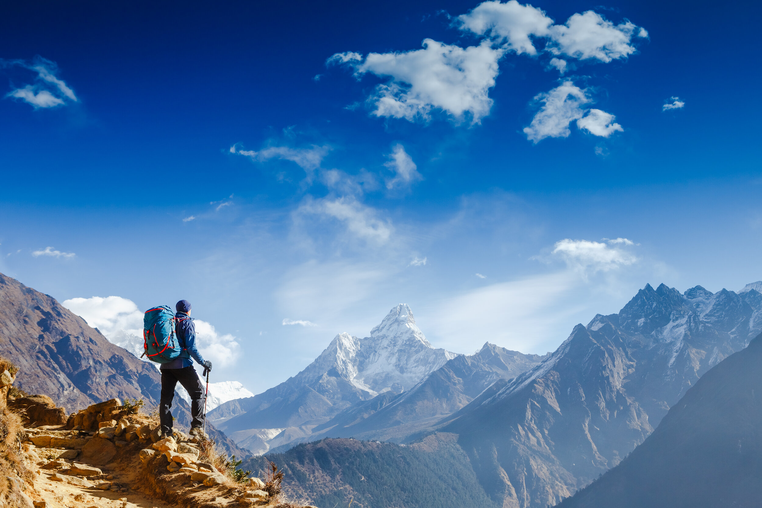 A hiker standing on a cliff in a mountainous region.