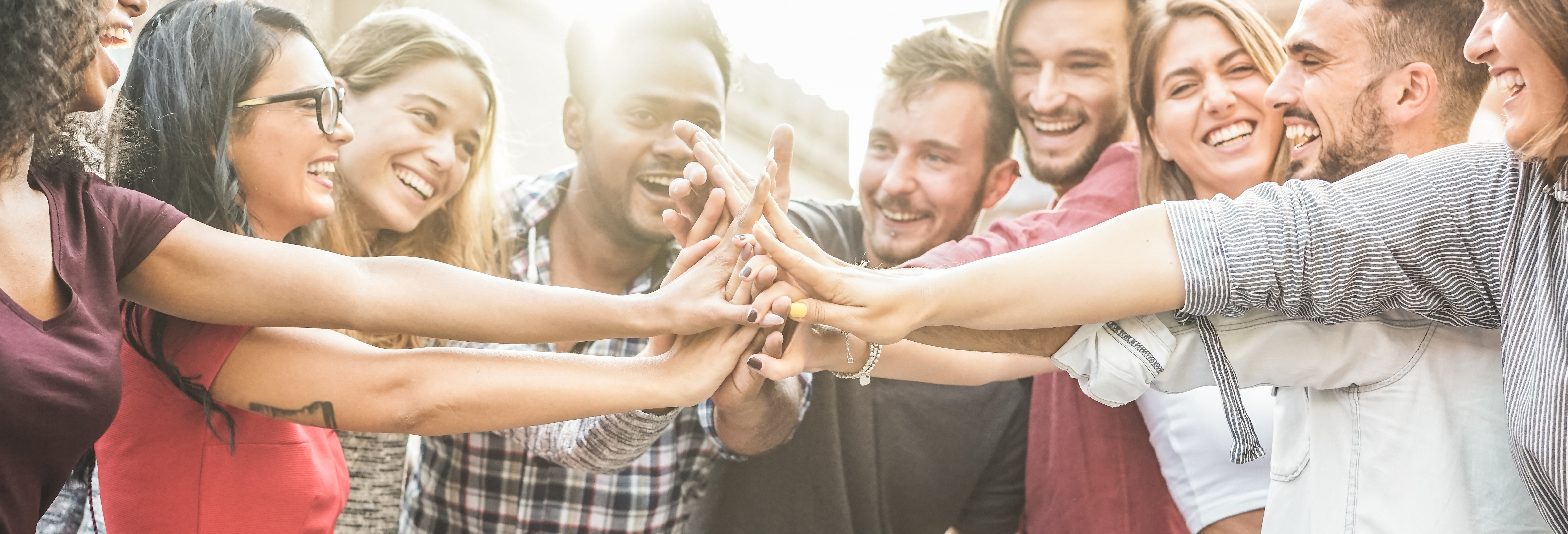 group of smiling friends with hands in the middle