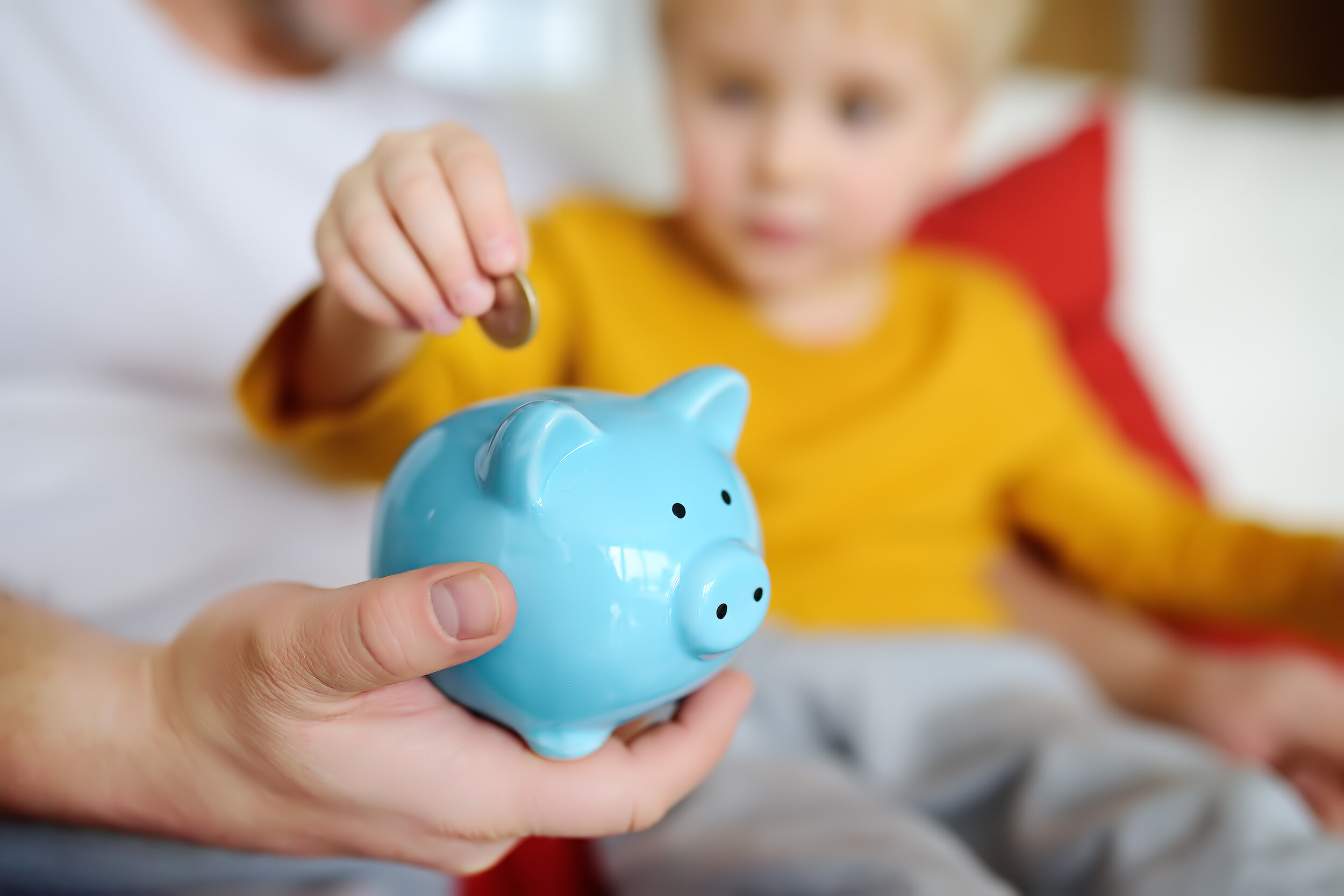 A toddler adding a coin into a piggy bank.