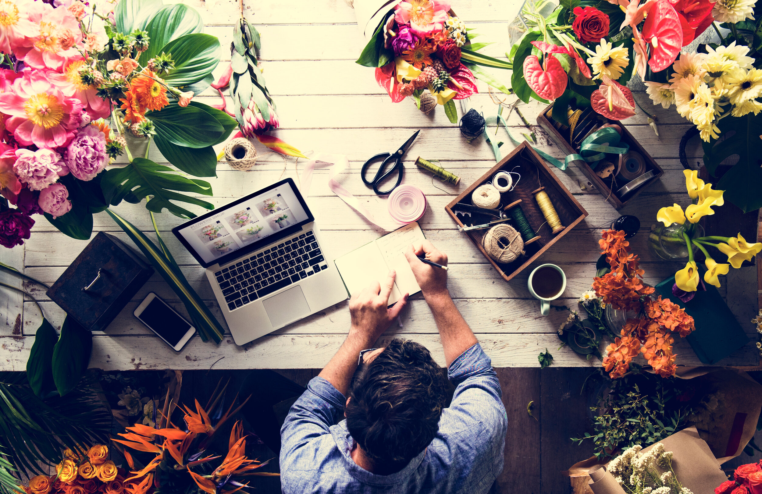 A business owner writing notes down on a table covered in vases of flowers.
