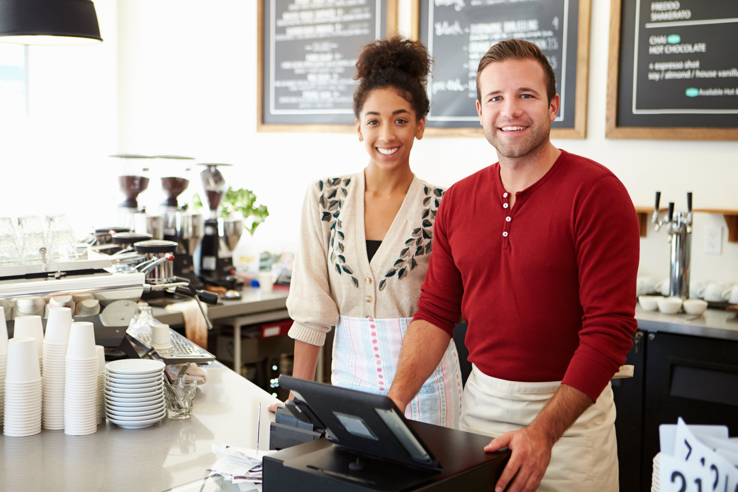 Two business owners at a cash register in a coffee shop.