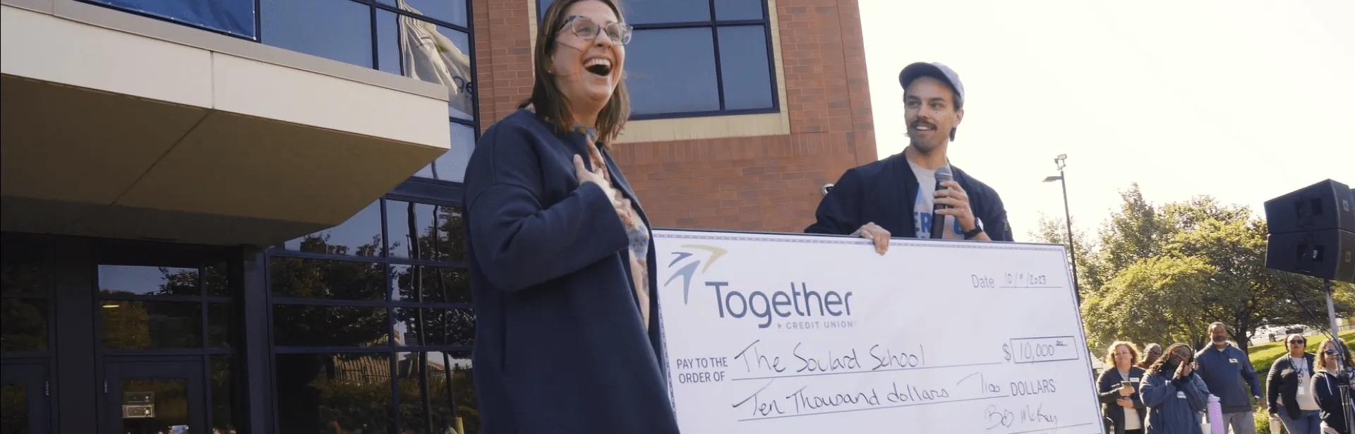 Two people in front of an office building holding a giant check that has the Together Credit Union logo on it.